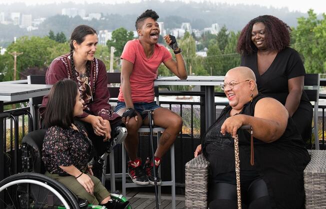 'Five people, some with visible disabilities, hanging out on a rooftop deck while talking and laughing.'