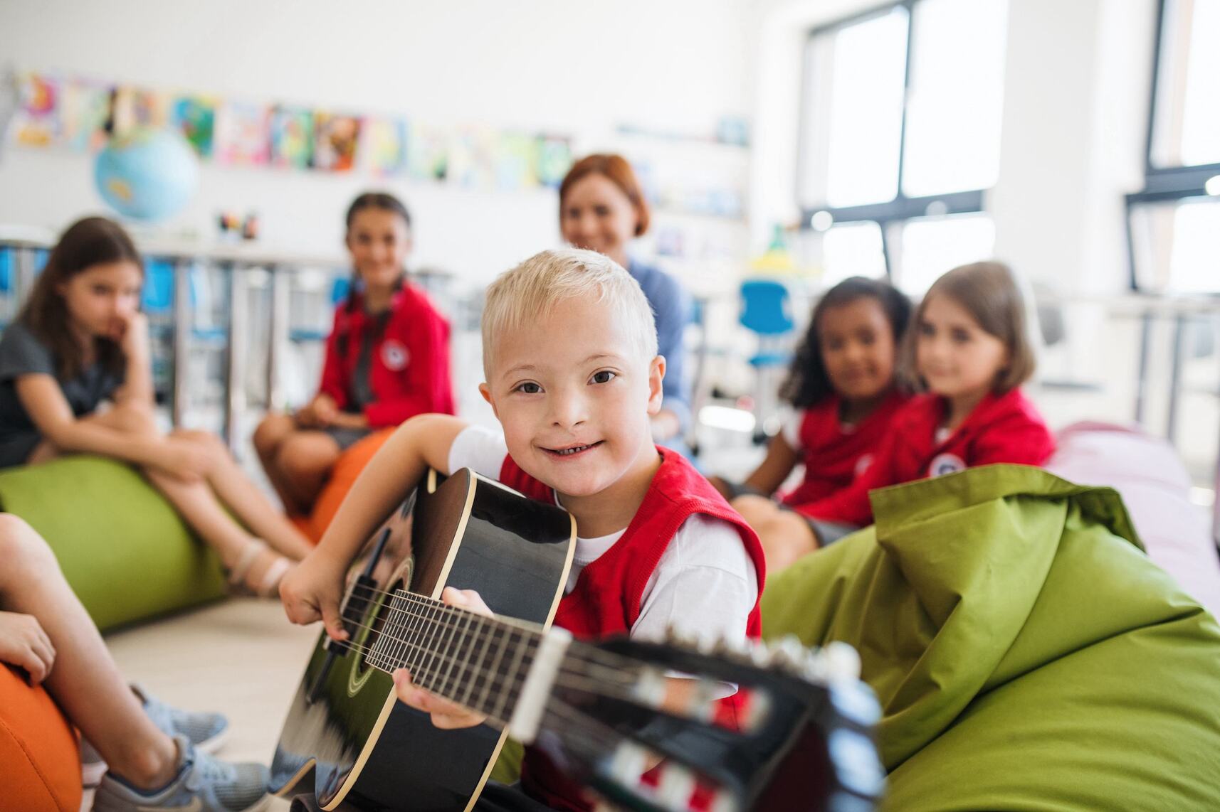 a child with down-syndrome is playing guitar and sitting with kids and a teacher