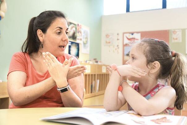 A teacher and a student sitting at a table signing to one another