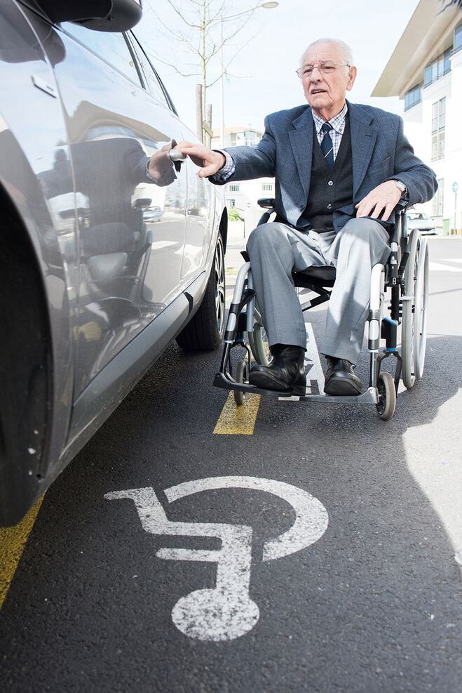 A man in a wheelchair approaching a vehicle with his hand on the door handle