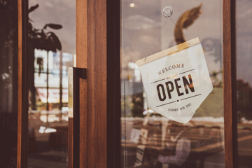 A sign hanging inside a storefront window reads Welcome. We are Open. Please come in