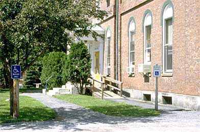 A photograph of the front of building showing an accessible parking space, accessible route and ramp to the entrance.