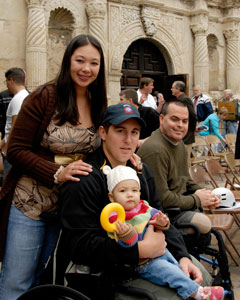 Photo: A man sits in a wheelchair with a woman standing behind him, her hands on his shoulders. A baby sits in his lap.