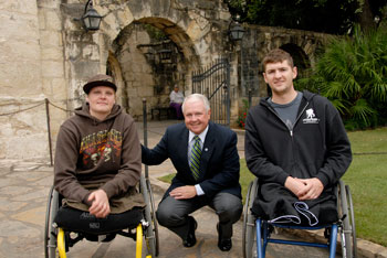 Photo: General Hornburg squats between two service members sitting in wheelchairs, both of whom have double leg amputations.