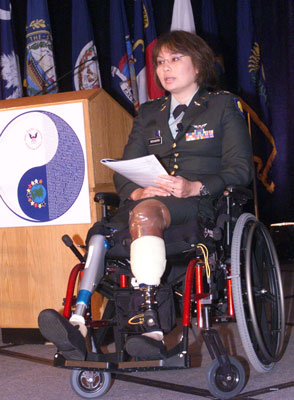 Photo of Assistant Secretary Duckworth, who sits in a wheelchair alongside a podium, has two prosthetic legs.